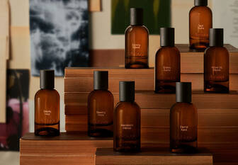 Amber Aesop fragrance bottles arranged on stepped wooden blocks before layered botanical and abstract images.