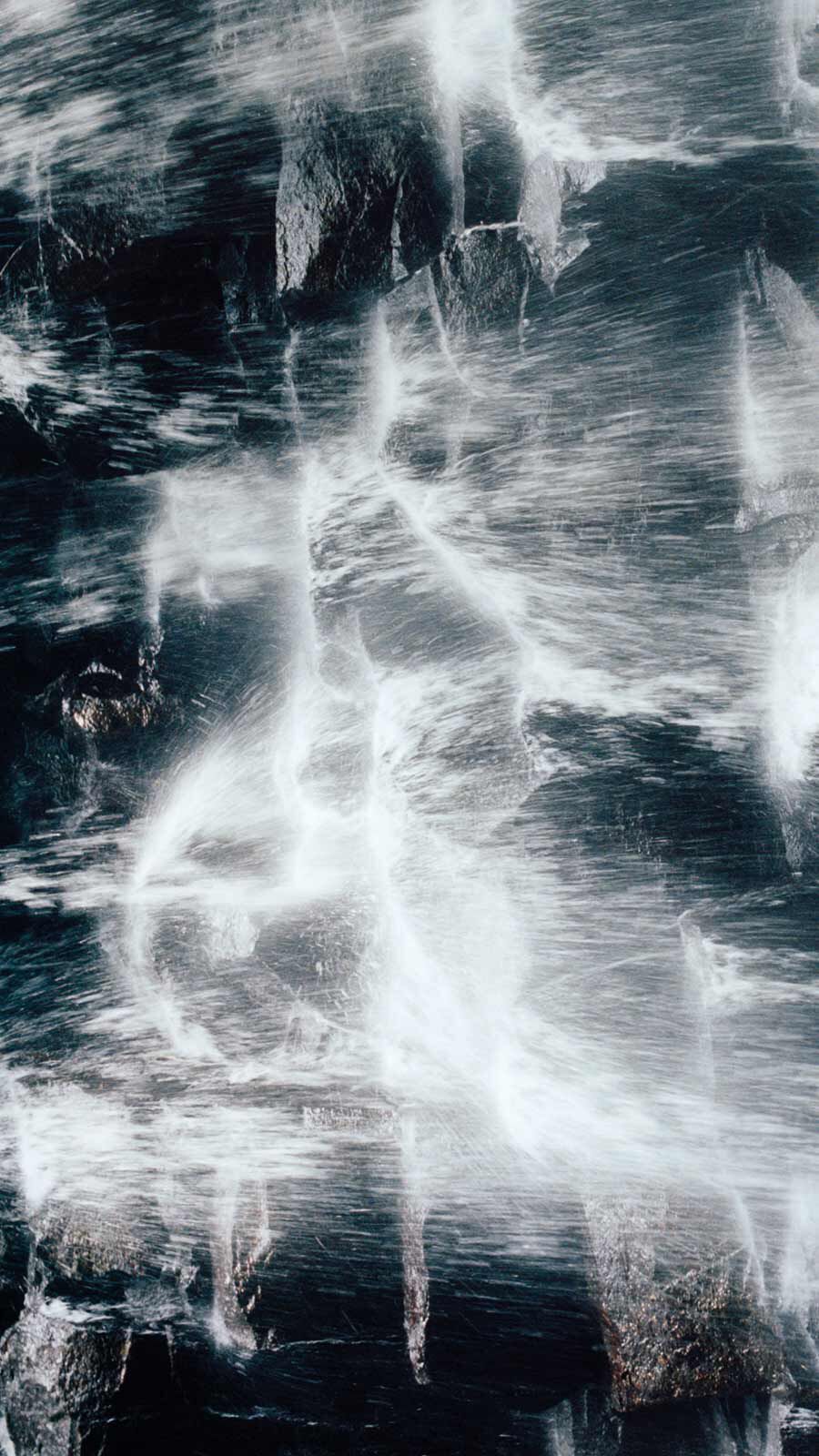 Close-up of rushing white water flowing over dark blue-grey rocks.