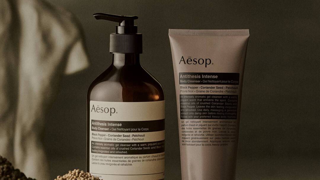 Aesop Antithesis Intense Body Cleanser pump bottle and tube beside piles of black peppercorns and coriander seeds.